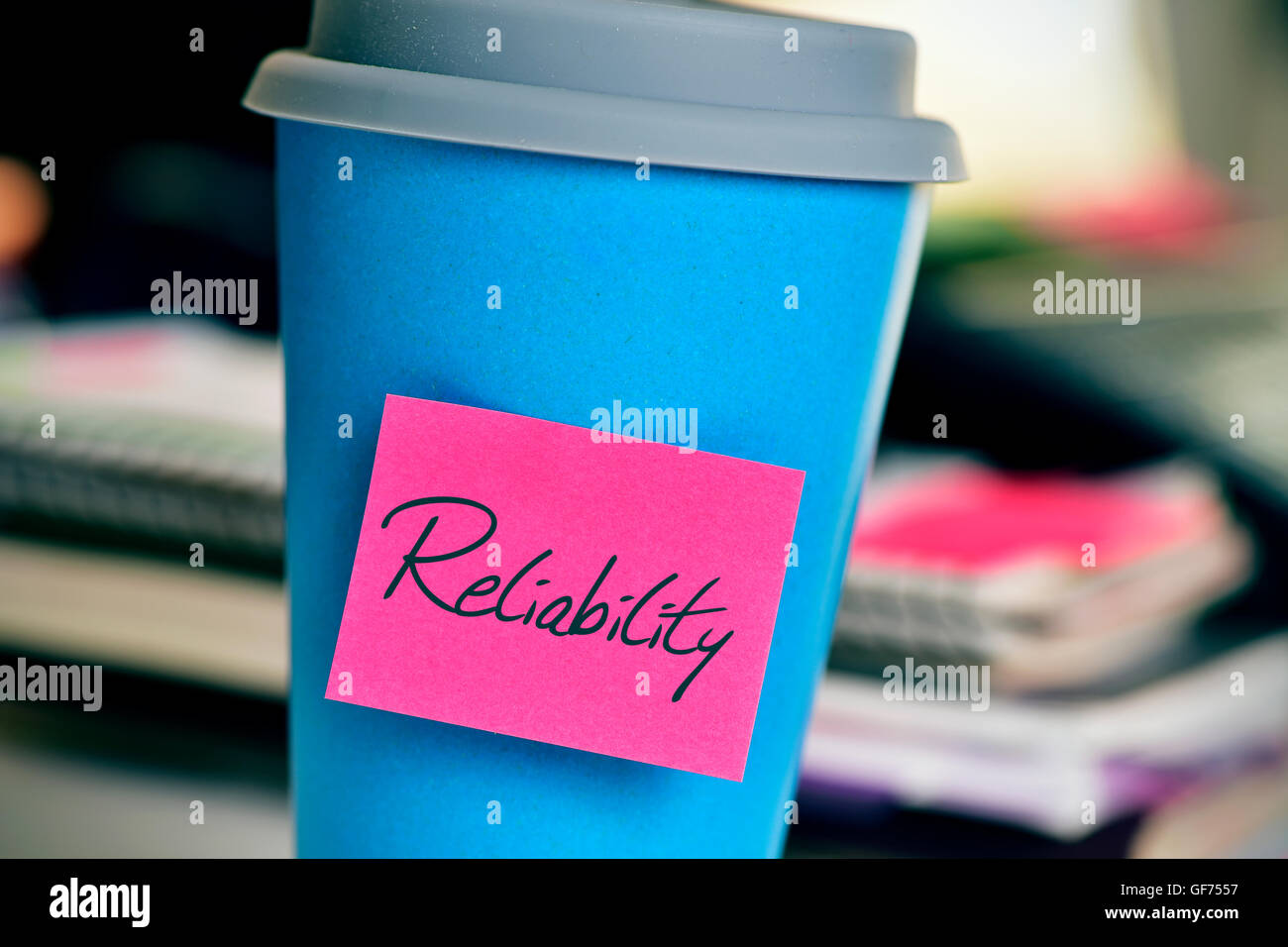 closeup of a pink sticky note with the word reliability in a blue cup of coffee or tea on an office desk Stock Photo