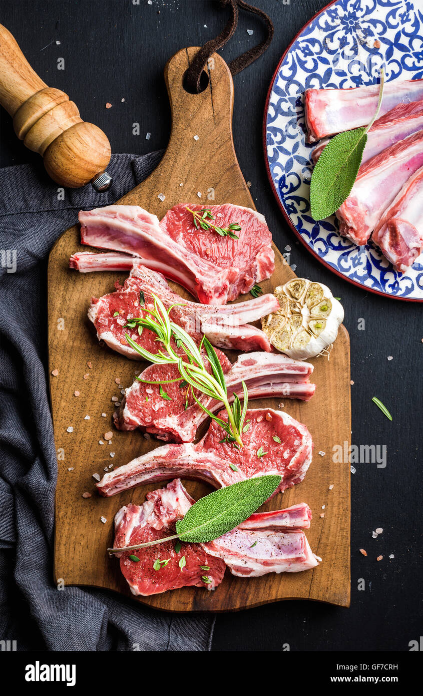 Raw uncooked lamb chops with herbs and spices on rustic wooden board