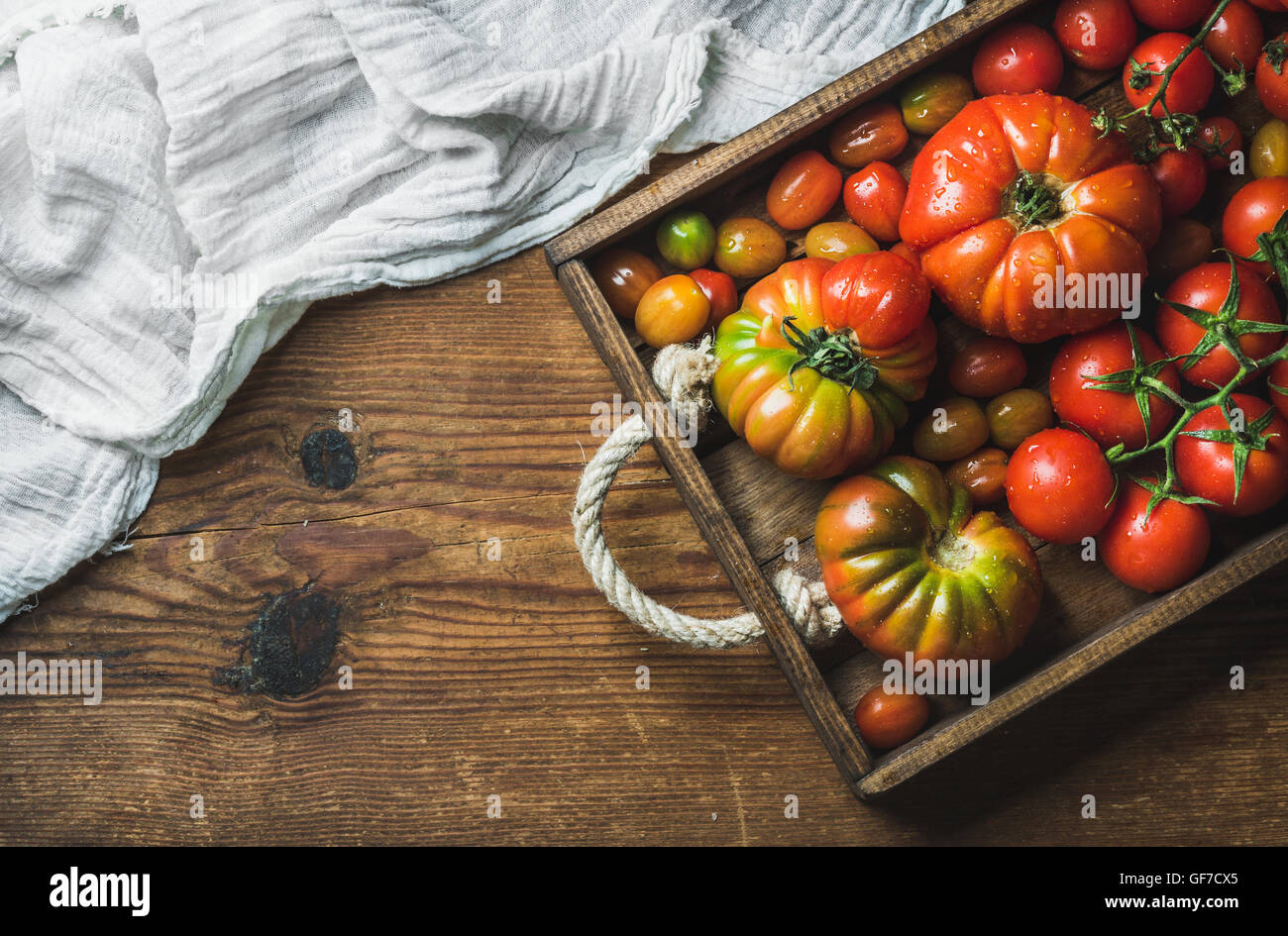 Colorful tomatoes of different sizes and kinds in dark wooden tray over ...
