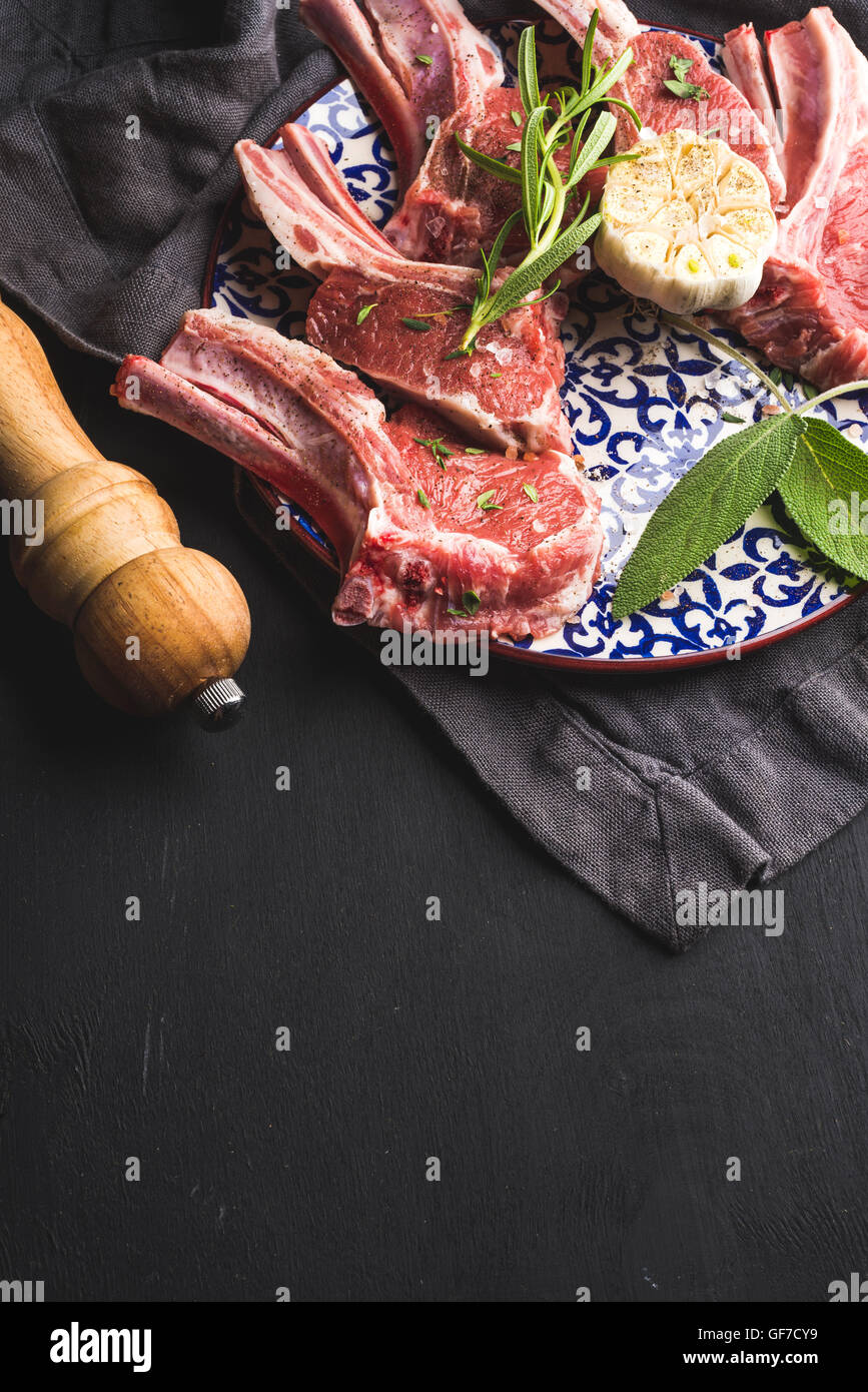 Raw uncooked lamb chops with herbs and spices on bright plate over dark