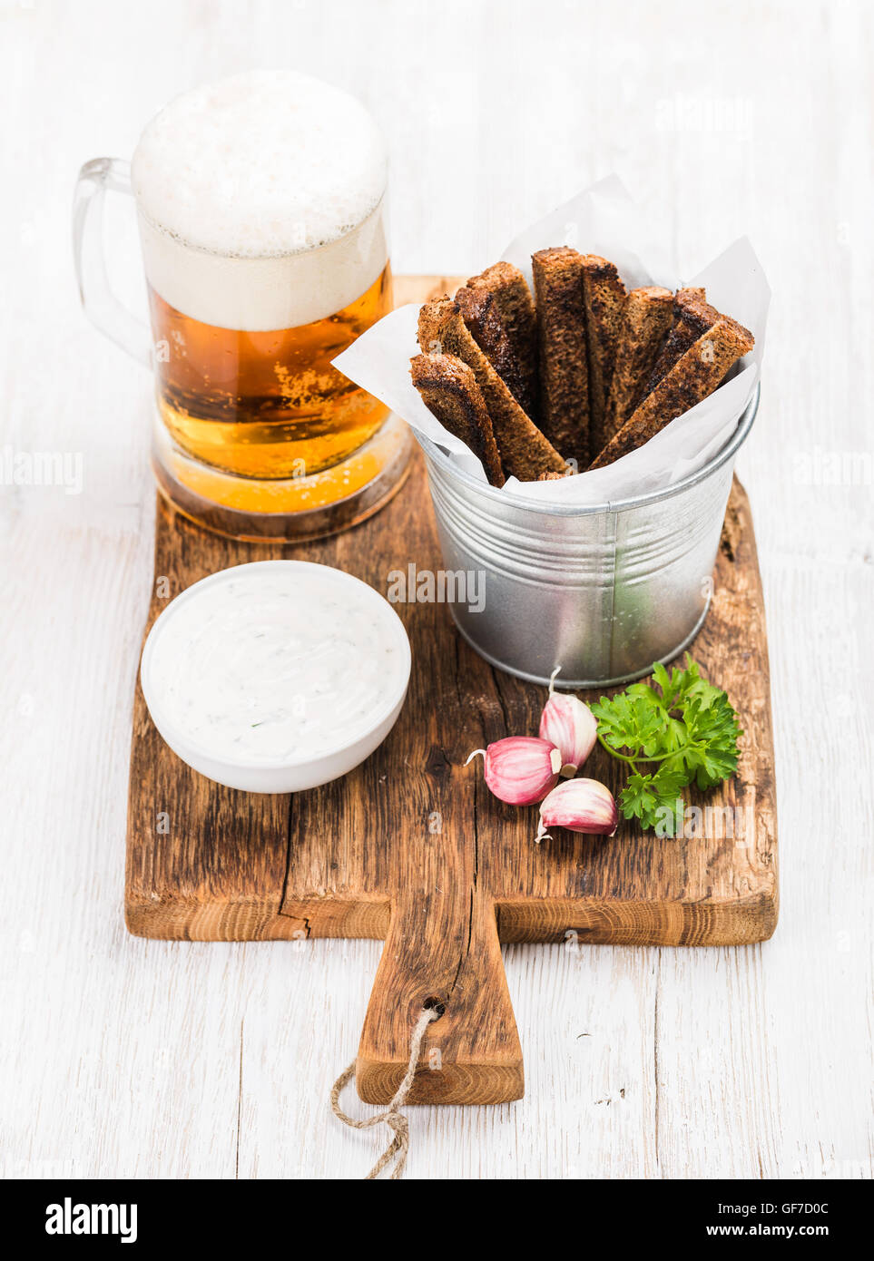 Beer snack set. Pint of pilsener in mug, open glass bottle, rye bread croutons with garlic cream cheese sauce and fresh parsley on rustic wooden board over white painted old background Stock Photo