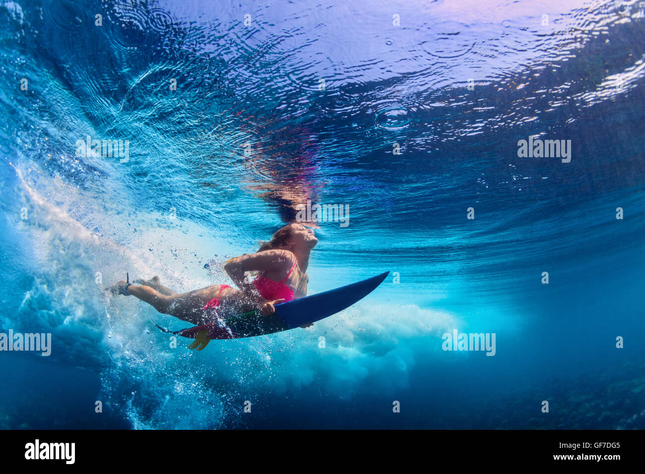 Young active girl wearing bikini in action - surfer with surf board dive underwater under big atlantic ocean wave. Stock Photo