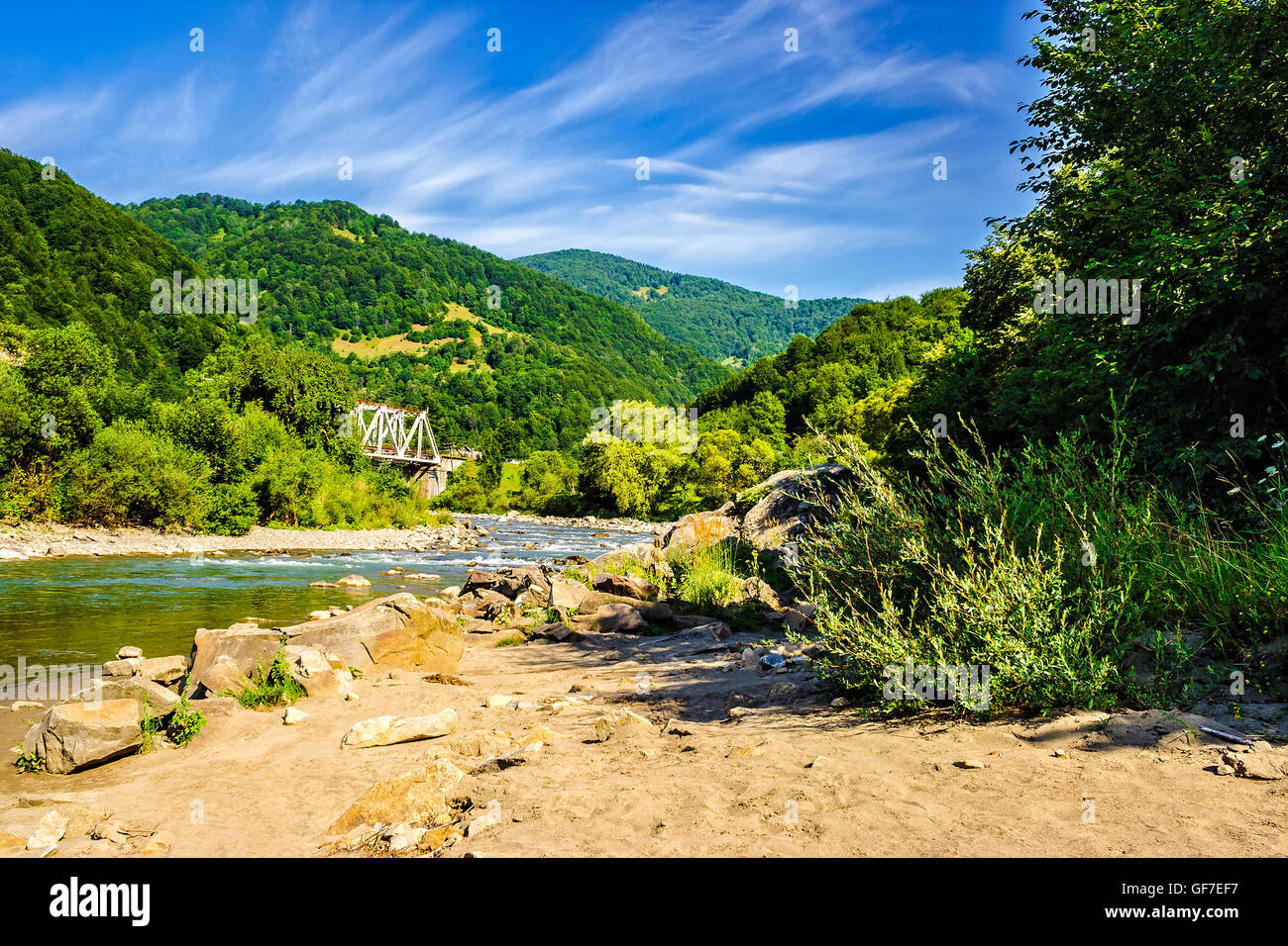 shore of a mountain river with stones and iron bridge among the forest in fural area Stock Photo