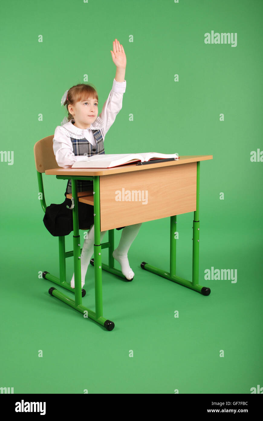 Girl in a school uniform sitting at a desk isolated on green background ...