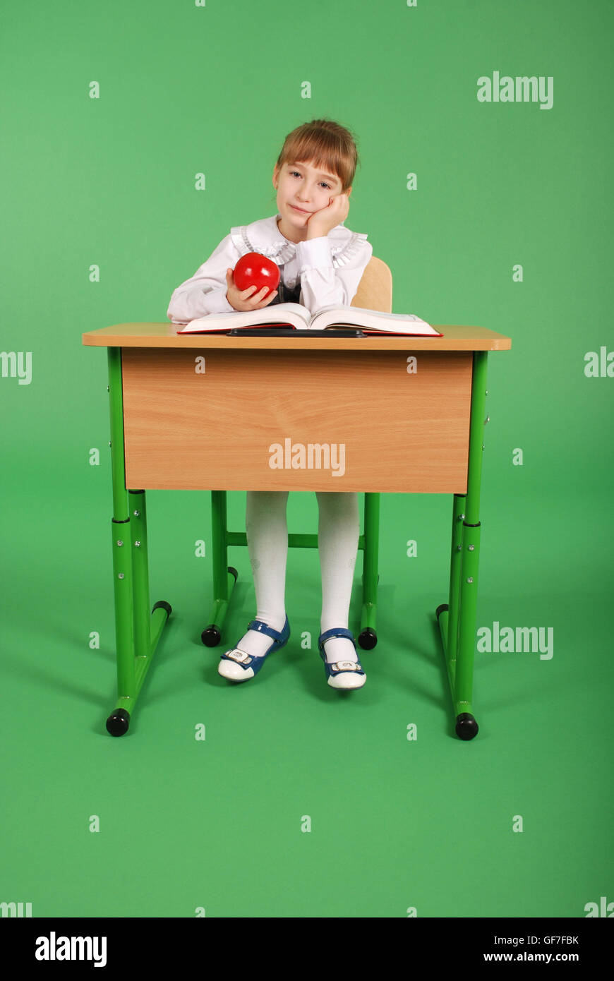 Girl in a school uniform sitting at a desk and reading a book isolated ...