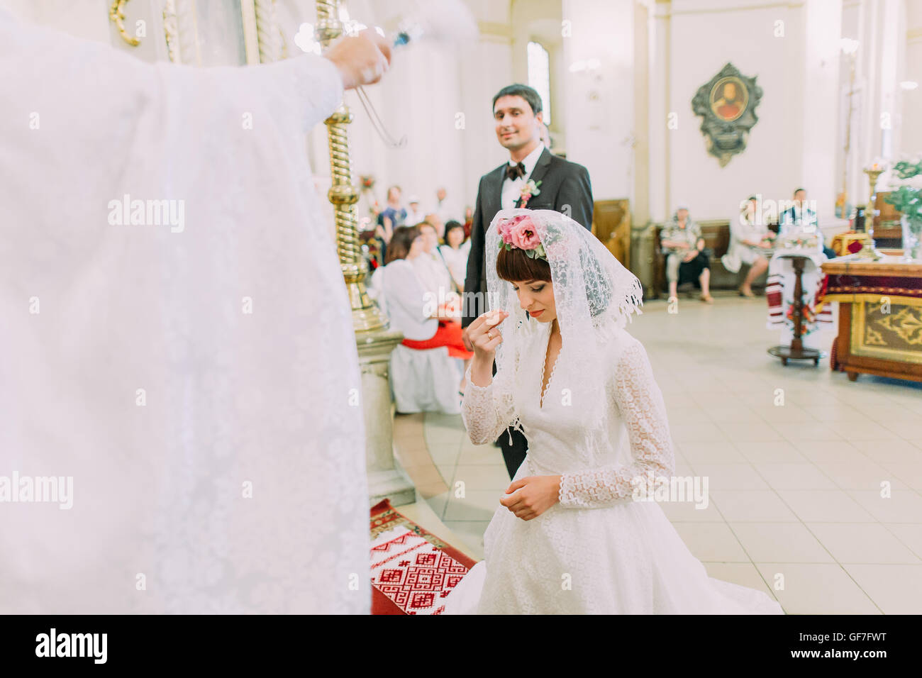 Bride prays on the knees standing in the front of priest in the church Stock Photo