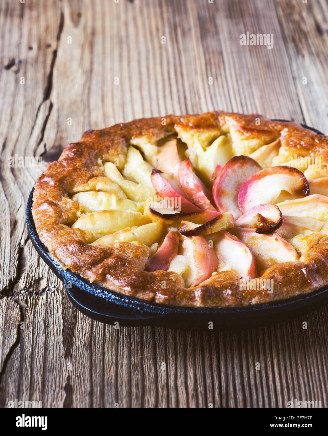 Homemade apple pie cooked in a frying pan and ripe apples on rustic