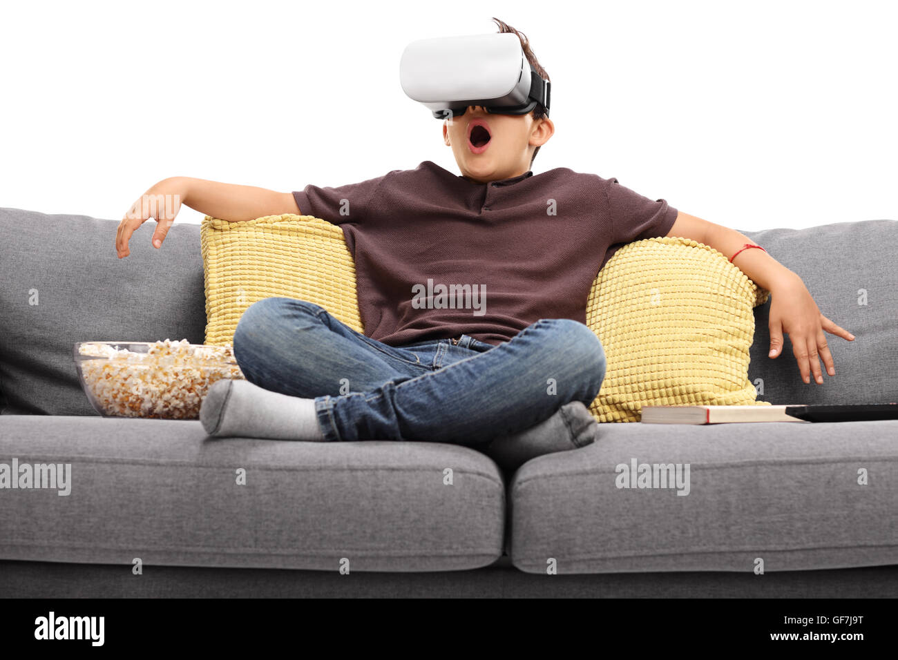 Astounded little kid using virtual reality goggles seated on a sofa isolated on white background Stock Photo