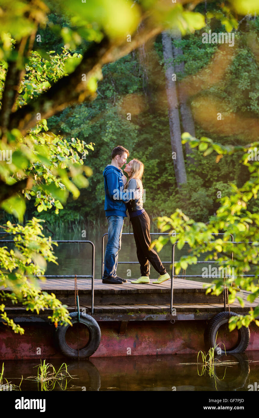 Man hugging his girlfriend at sunset on pier near water Stock Photo