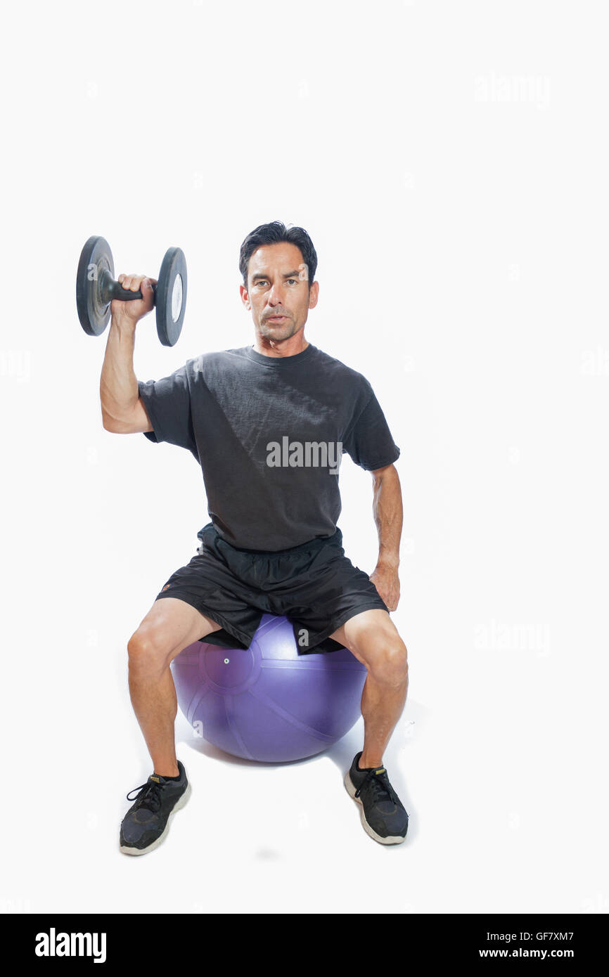 Middle age man tired from single dumbbell press seated on ball with weighted vest. Stock Photo