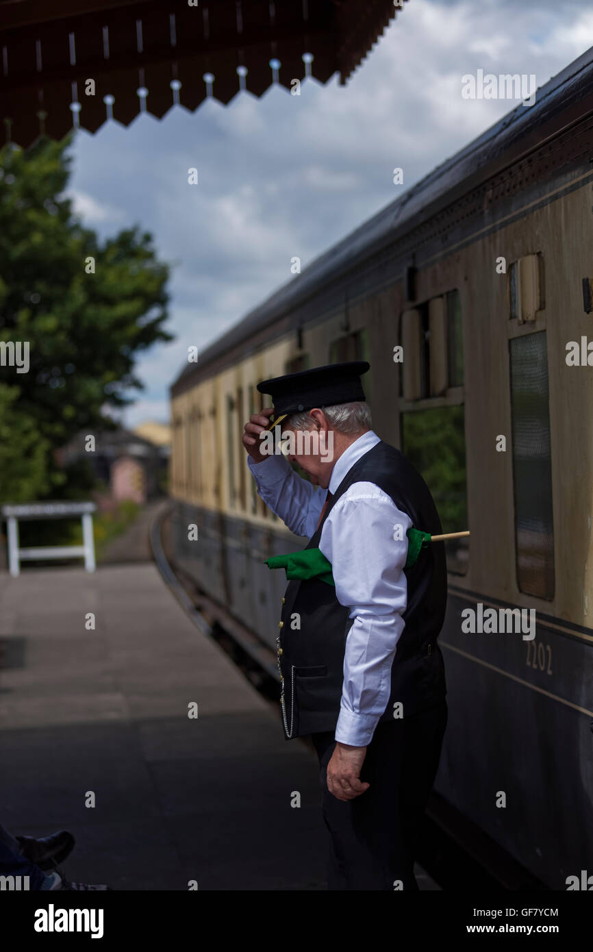 Train guard in uniform on the platform tipping cap at a passenger out