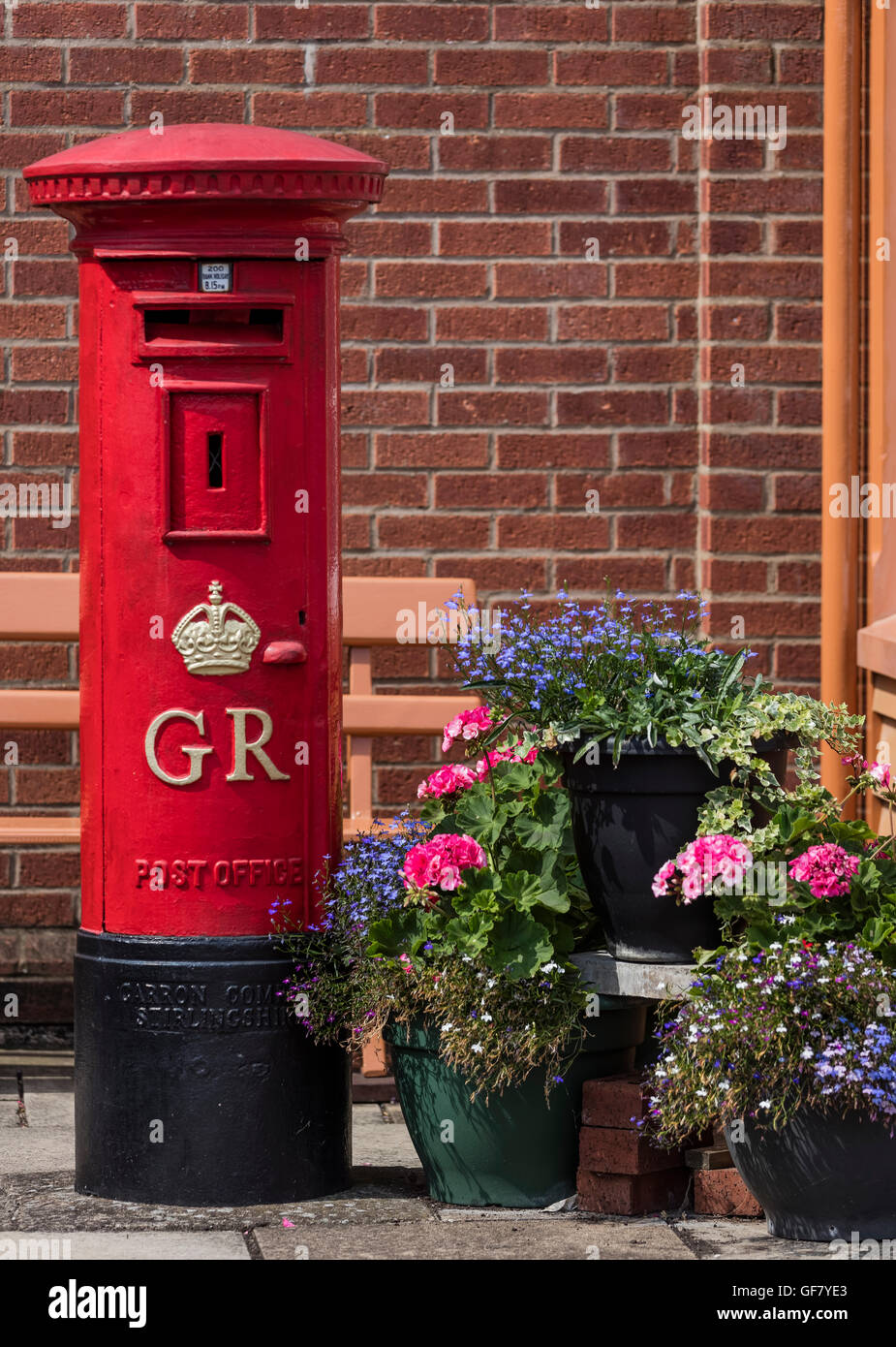 Old fashioned red post box used in the reign of King George VI next to hanging baskets with flowers at the Didcot Railway Centre Stock Photo