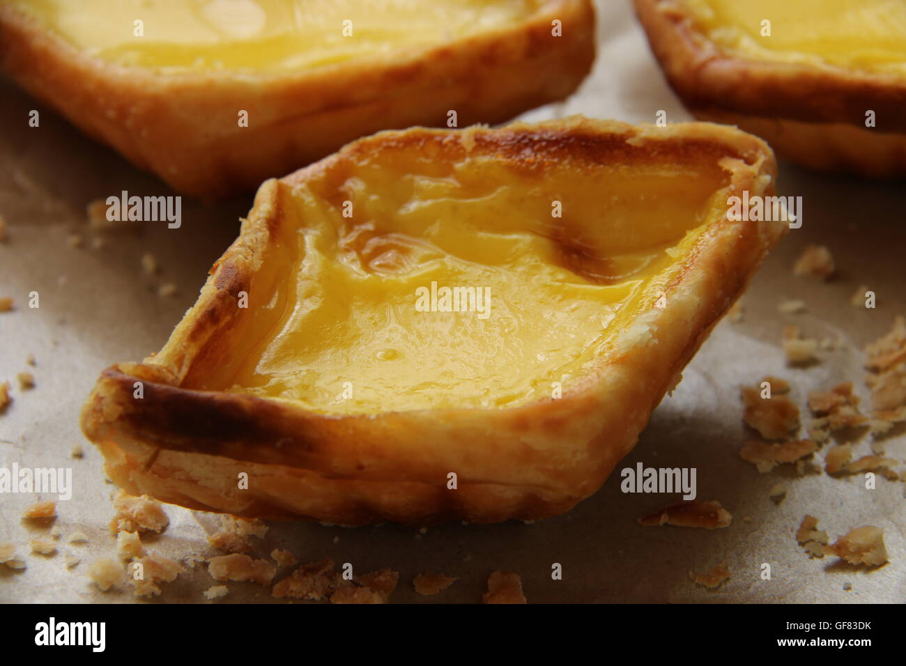 Egg tarts arranged on crumpled food wrapping paper. The crumbs are scattered around the tarts. Stock Photo