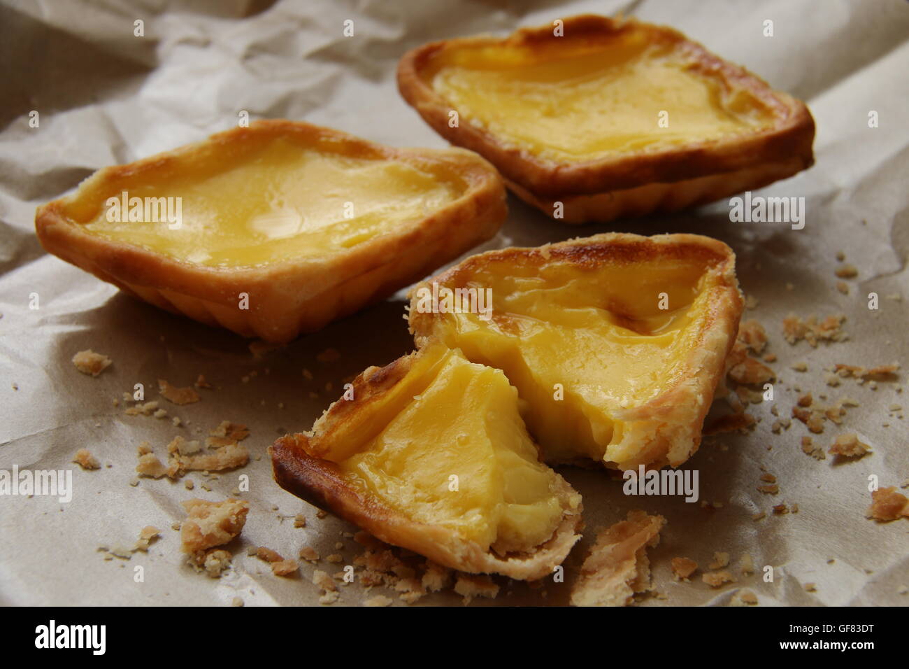 Egg tarts arranged on crumpled food wrapping paper. The crumbs are scattered around the tarts. Stock Photo