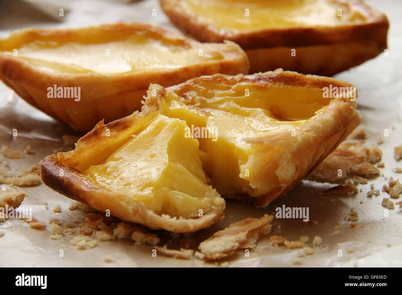 Egg tarts arranged on crumpled food wrapping paper. The crumbs are scattered around the tarts. Stock Photo