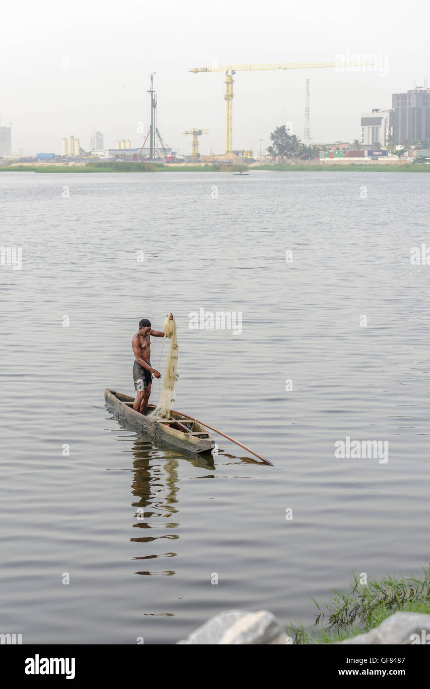 Fisherman in dugout canoe holding net, fishing in Kuramo Waters with Eko Atlantic development background. Lagos, Nigeria, Africa Stock Photo