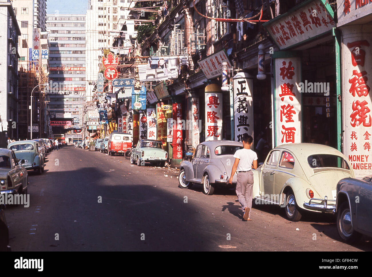1960s, historical, daytime and a view of a side street in the old town of Hong Kong, with chinese characters covering the concrete posts supporting the street buildings. Cars of the era are parked alongside. Stock Photo