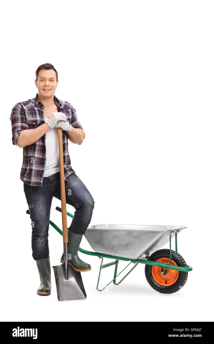 Full length portrait of a male worker holding a shovel and posing by an empty wheelbarrow isolated on white background Stock Photo