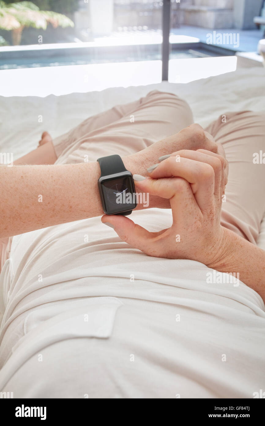 Closeup shot of woman checking time on her smart watch, she is lying on bed at home. Stock Photo