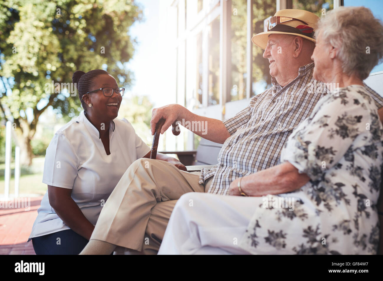 Portrait of senior couple relaxing on a bench outside their retirement home. Caucasian elderly man and woman sitting with female Stock Photo