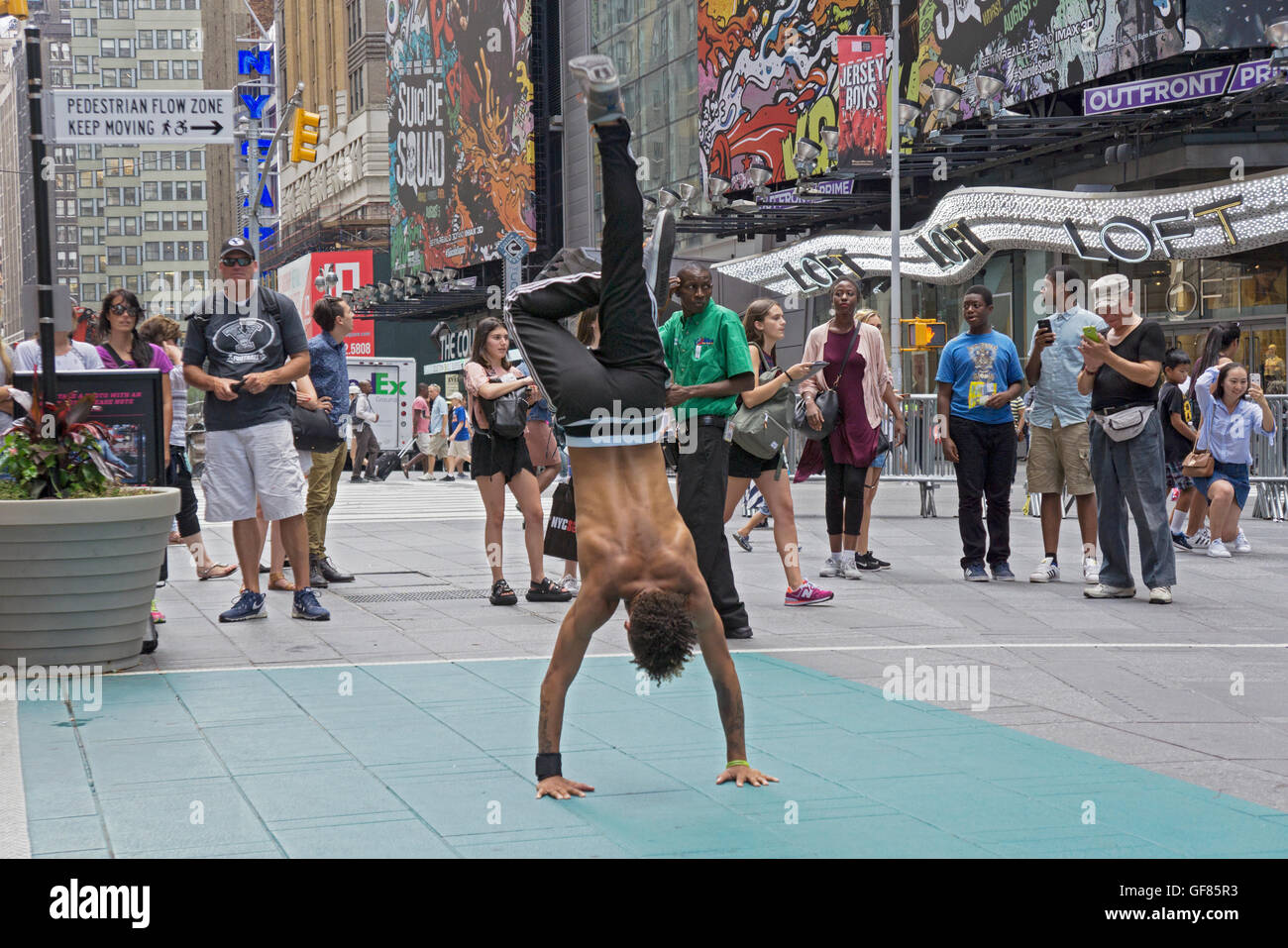 An acrobatic athletic street busker in Times Square does a handstand for a small group of tourists. New York City. Stock Photo