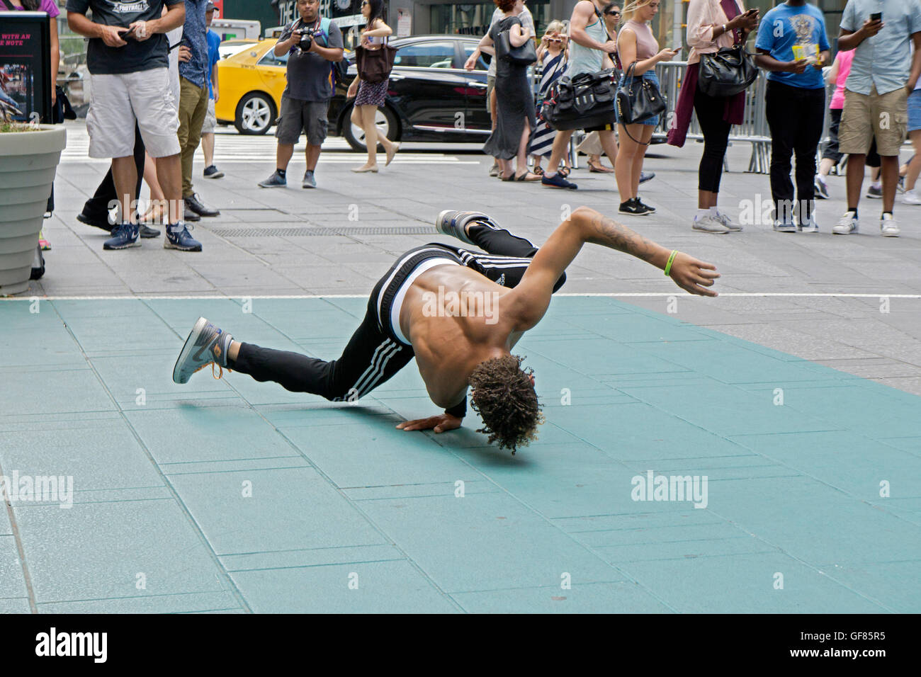 An acrobatic athletic street busker in Times Square does a hand stand for a small group of tourists. New York City. Stock Photo
