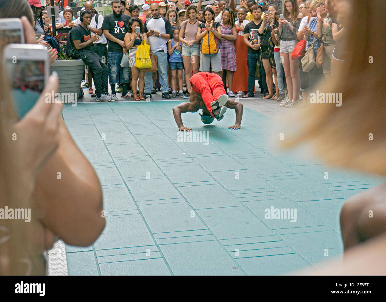 An acrobatic athletic street busker in Times Square does a handstand for a large crowd of tourists Stock Photo