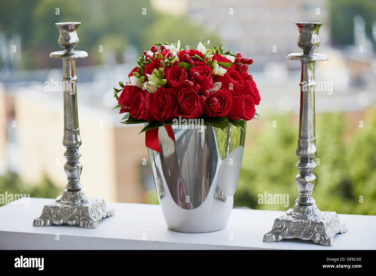 dense red bouquet of roses and berries, brilliant in the iron bucket and two metal candle holders Stock Photo