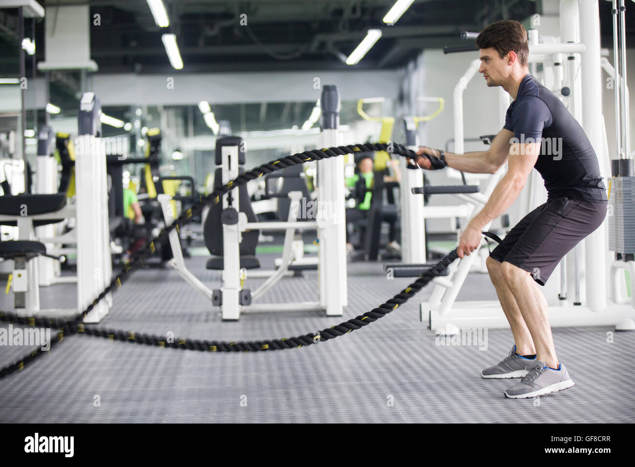 Young man exercising with battling rope at gym Stock Photo