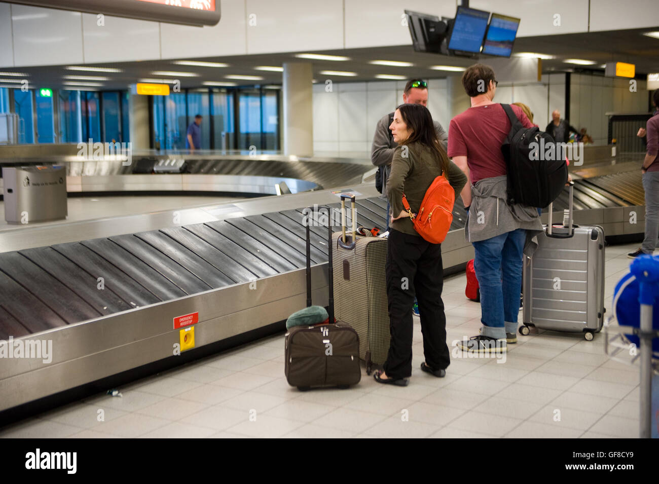 AMSTERDAM, THE NETHERLANDS - MAY 05, 2016: People are waiting on an airport at the luggage belt for their suitcases to arrive. Stock Photo