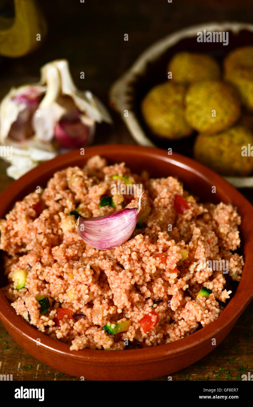 closeup of an earthenware casserole whit couscous with vegetables and some falafel in a plate in the background, on a wooden tab Stock Photo