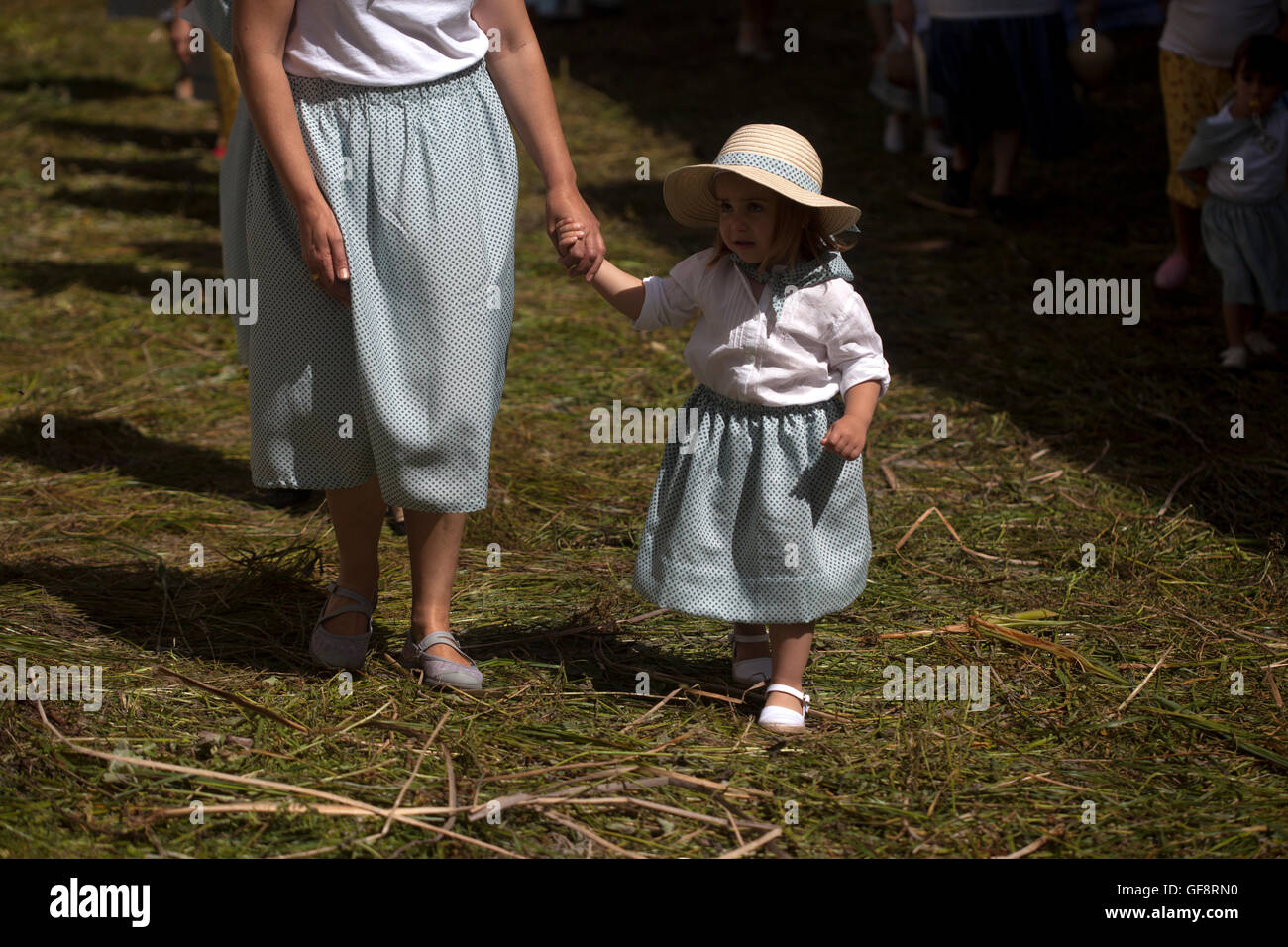 A woman holding the hand of his daughter, dressed as a harvester walk in a street covered by sedge during Corpus Christi religio Stock Photo