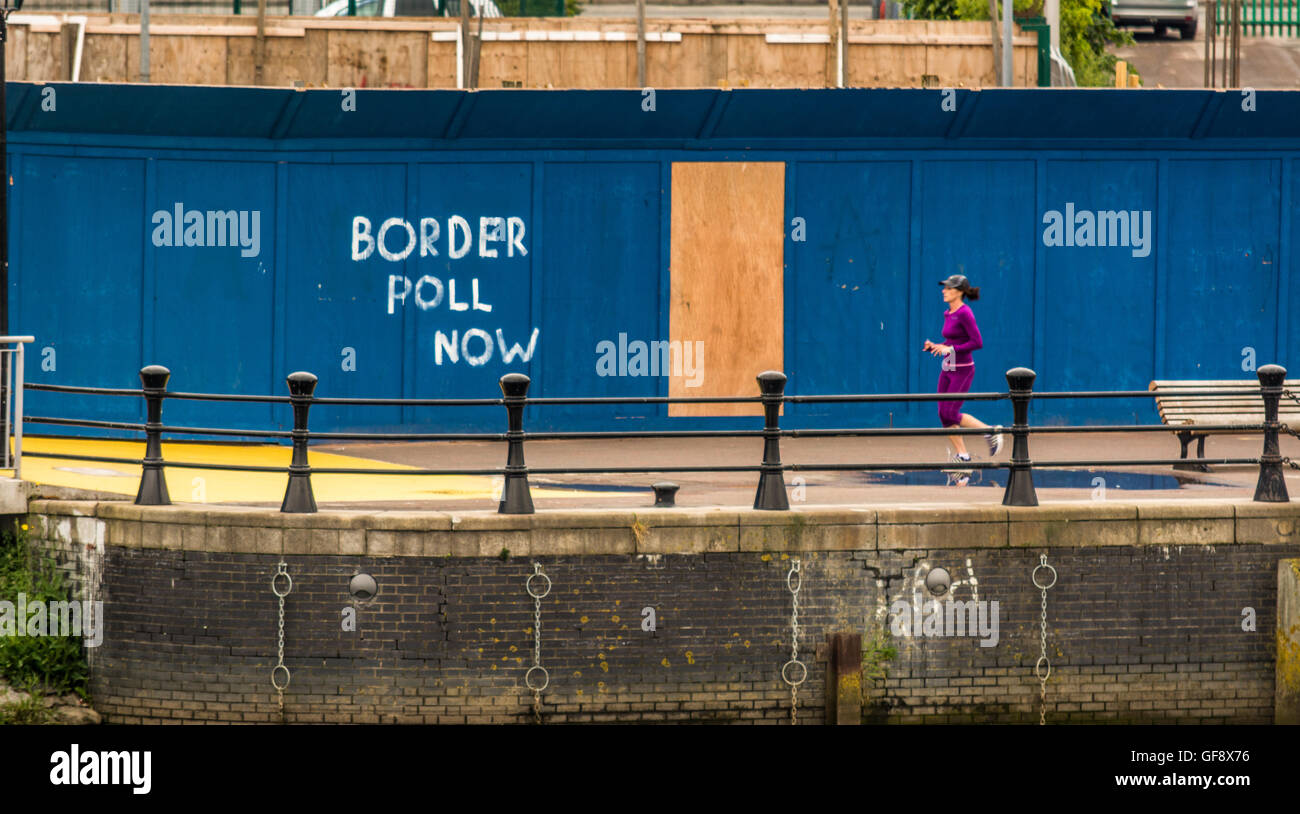 A jogger passing Border Poll Now graffiti in Belfast, along the River Lagan. Stock Photo