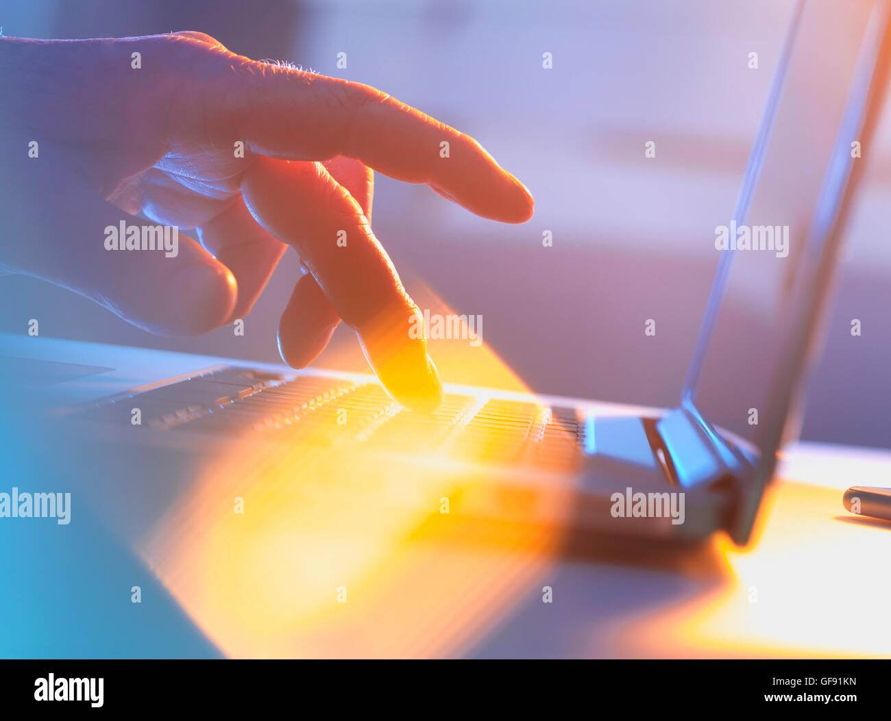 PROPERTY RELEASED. MODEL RELEASED. Close-up of silhouetted male hand typing on a laptop keyboard. Stock Photo