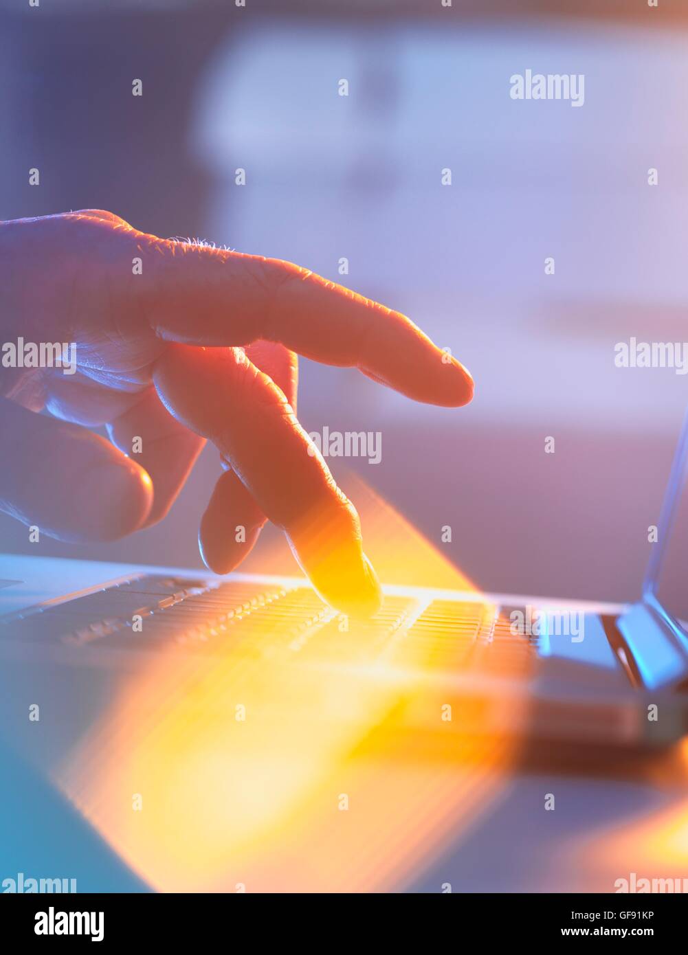 MODEL RELEASED. Close-up of silhouetted male hand typing on a laptop keyboard. Stock Photo
