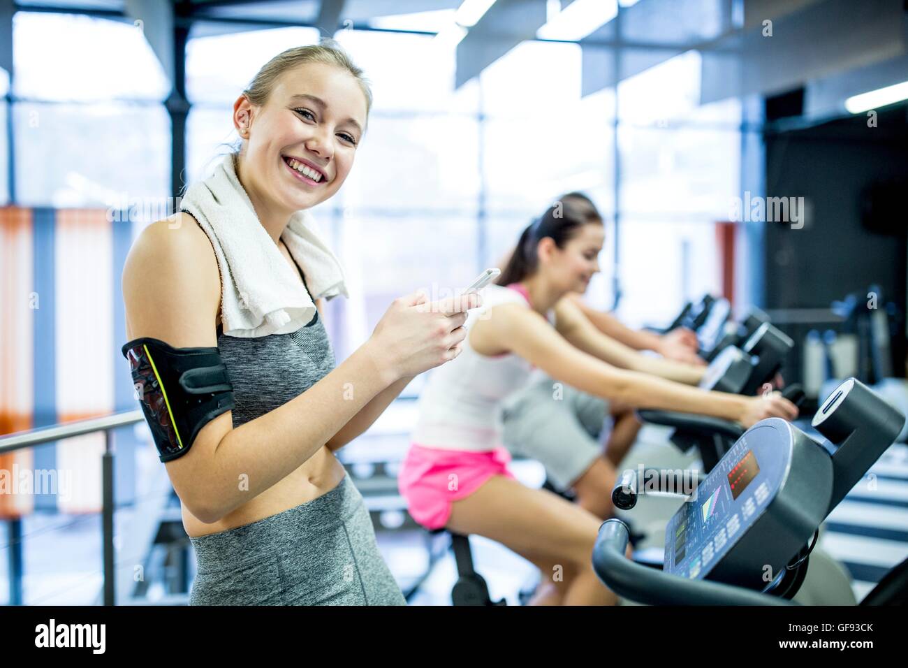 PROPERTY RELEASED. MODEL RELEASED. Portrait of young woman texting on mobile phone while work out in gym, smiling. Stock Photo