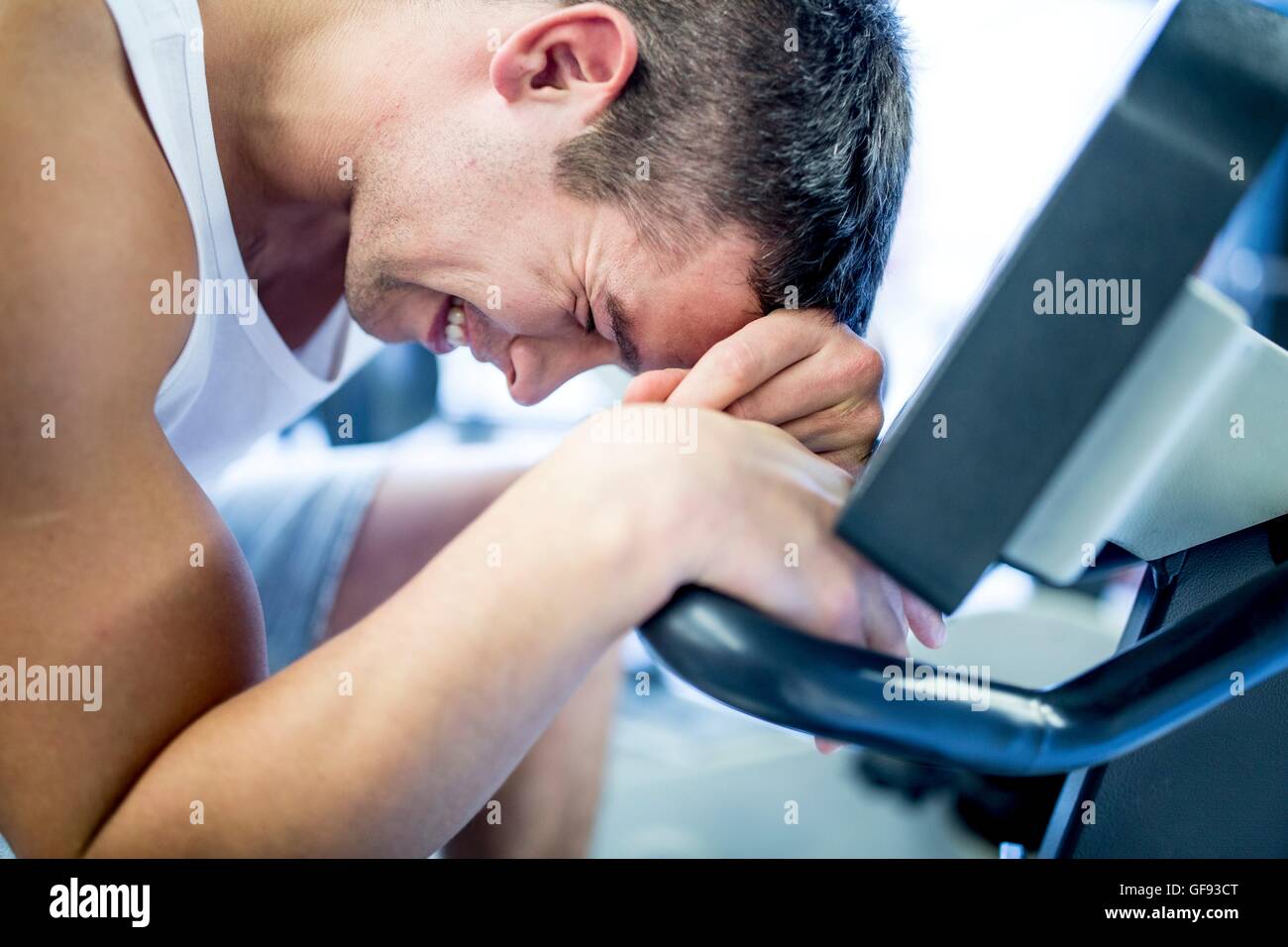 PROPERTY RELEASED. MODEL RELEASED. Close-up of young man resting his head on exercise machine in gym, smiling. Stock Photo