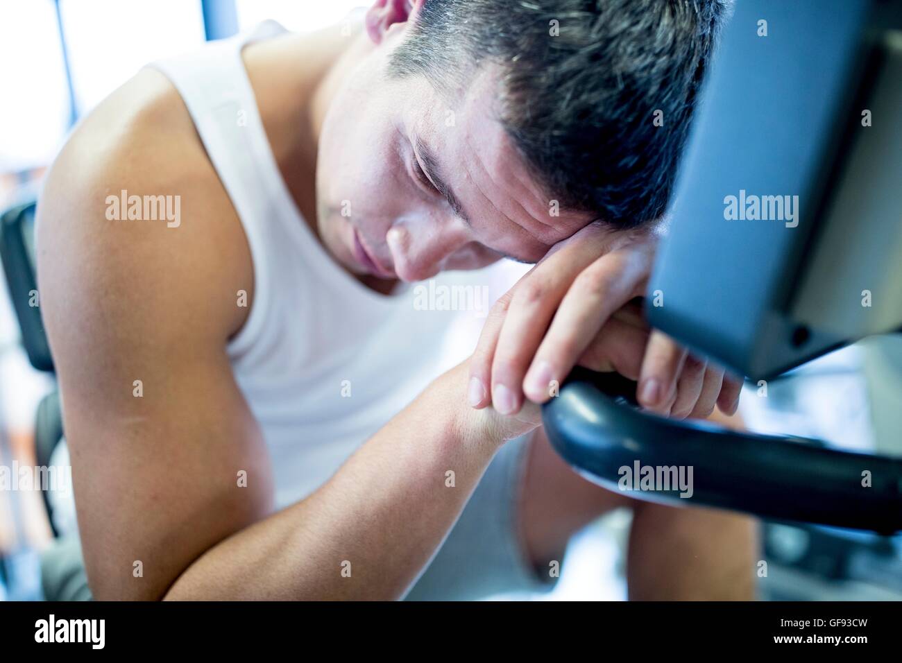 PROPERTY RELEASED. MODEL RELEASED. Close-up of young man resting his head on exercise machine in gym. Stock Photo