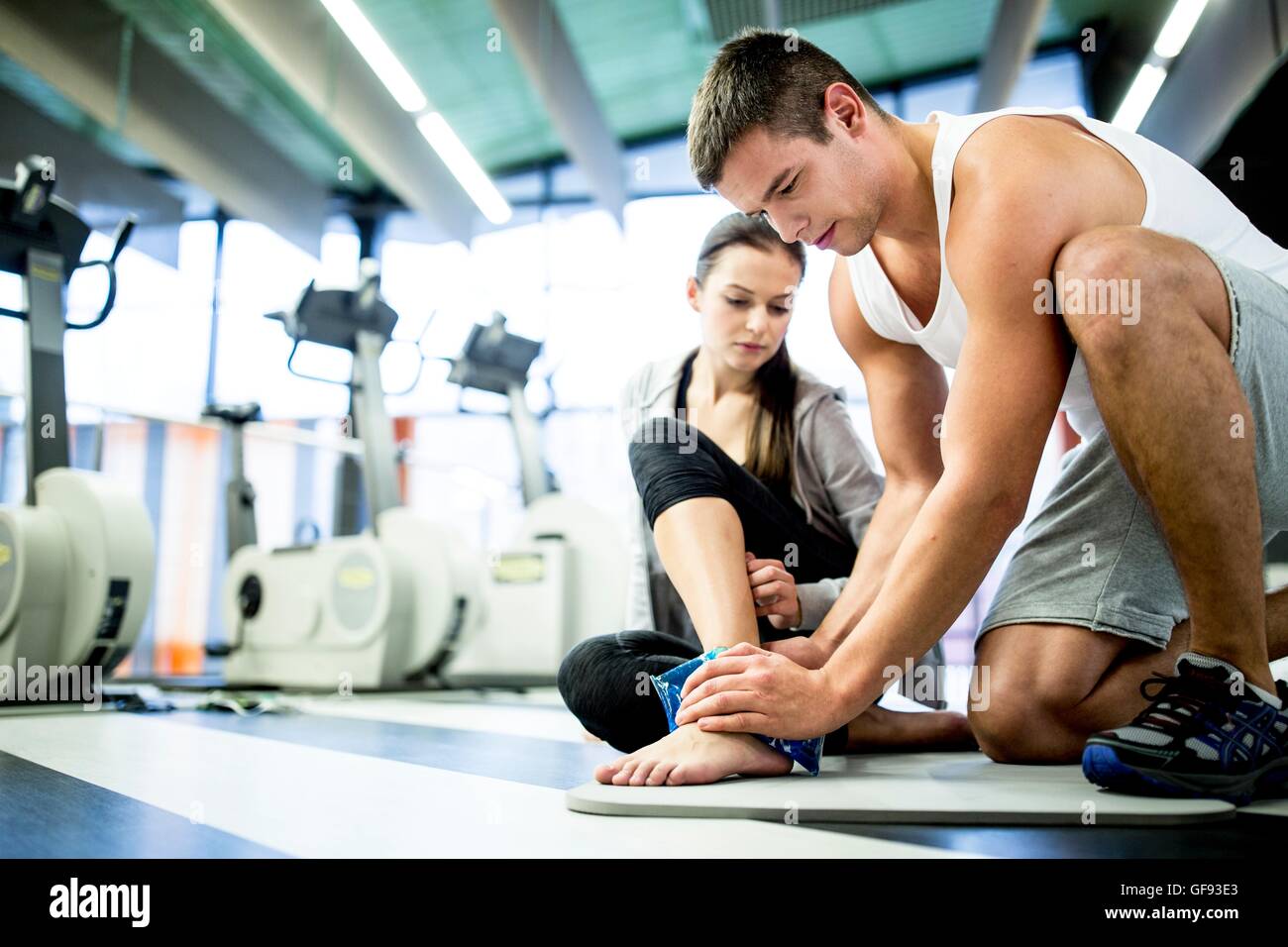 PROPERTY RELEASED. MODEL RELEASED. Young man applying ice pack on young woman's ankle in gym. Stock Photo