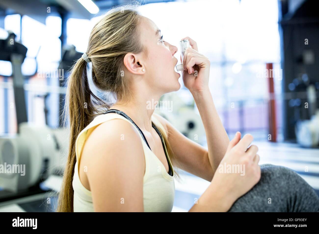 PROPERTY RELEASED. MODEL RELEASED. Young woman using inhaler in gym. Stock Photo
