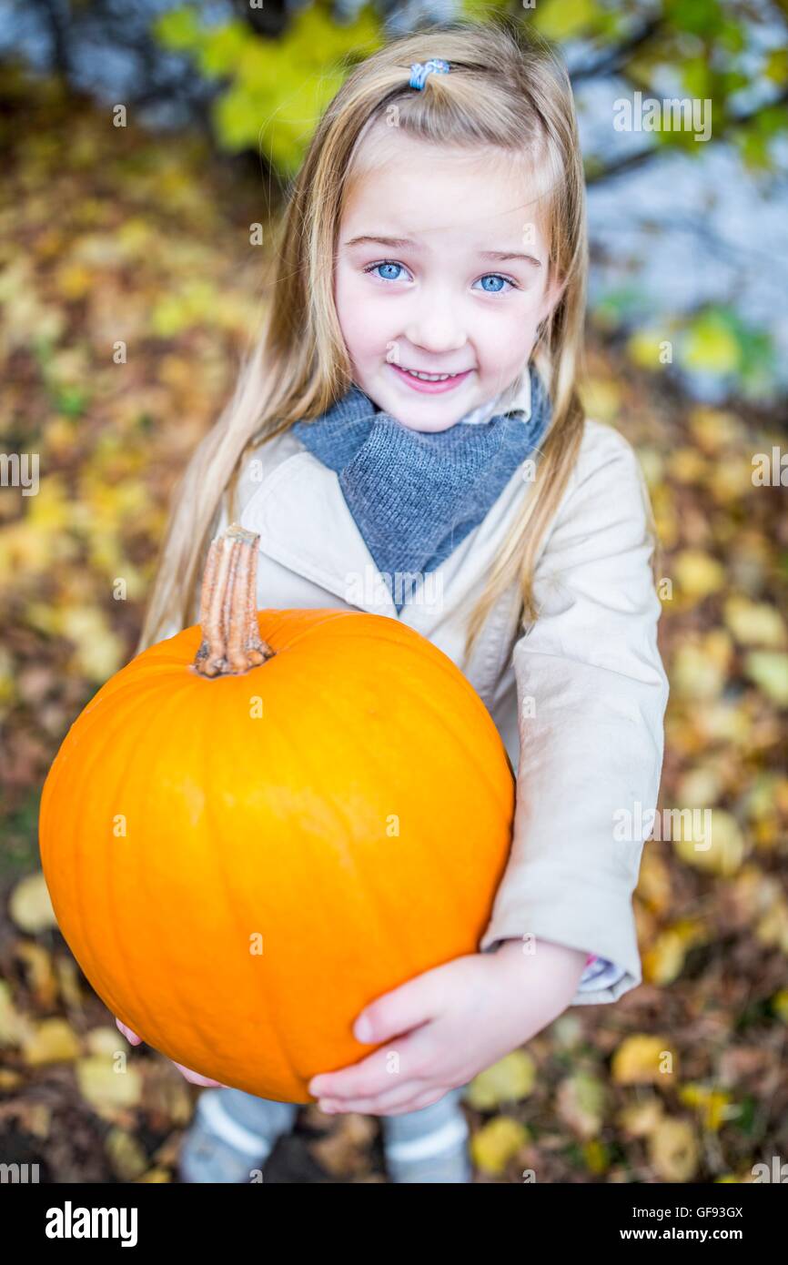 MODEL RELEASED. Blonde girl holding pumpkin in park, portrait, smiling. Stock Photo