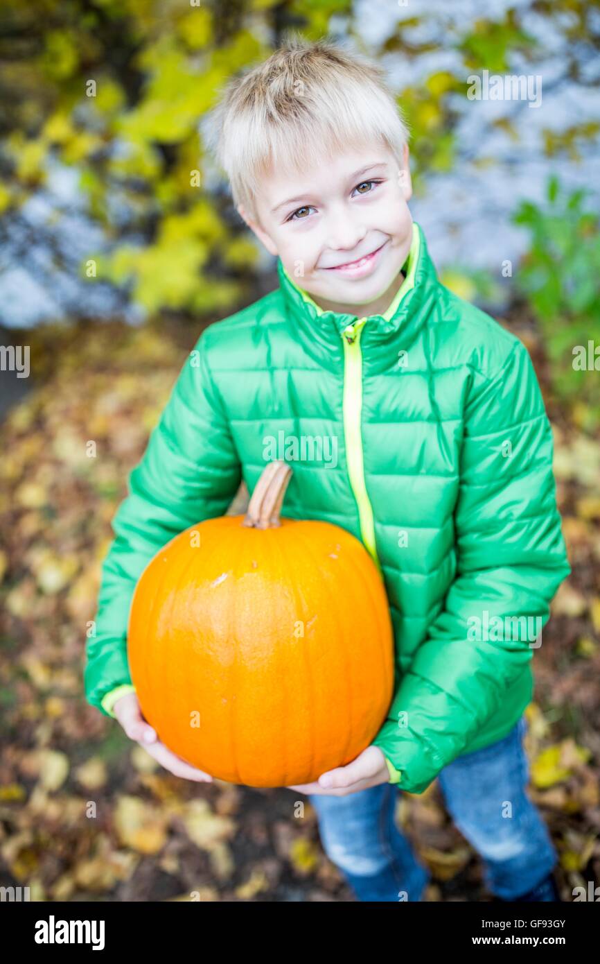 MODEL RELEASED. Blonde boy holding pumpkin in park, portrait, smiling. Stock Photo
