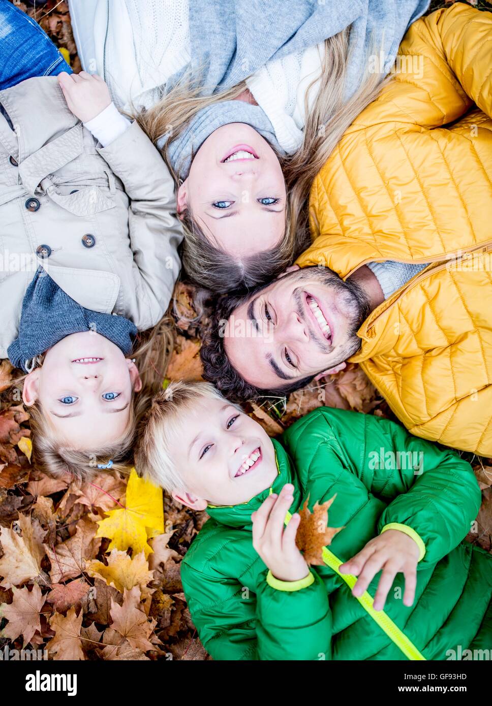 MODEL RELEASED. Family lying on dried leaves in autumn and smiling, portrait. Stock Photo