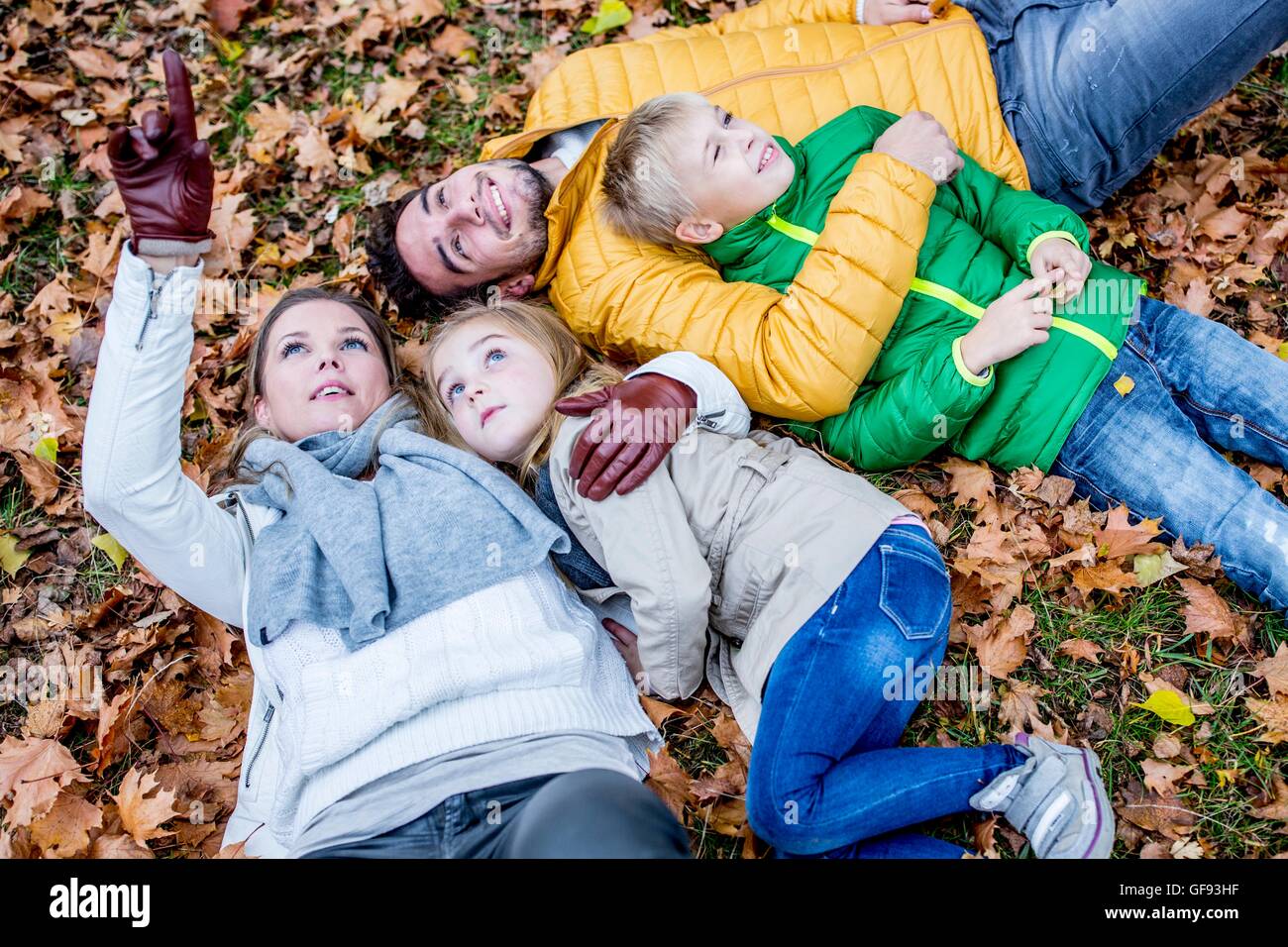 MODEL RELEASED. Family lying on dried leaves in autumn and smiling, mother pointing upwards. Stock Photo