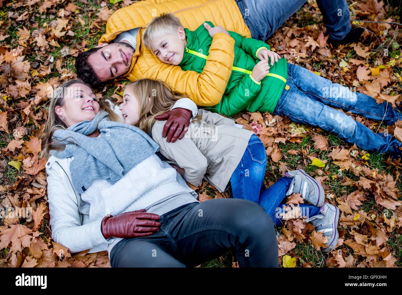 MODEL RELEASED. Family lying on dried leaves in autumn and talking. Stock Photo