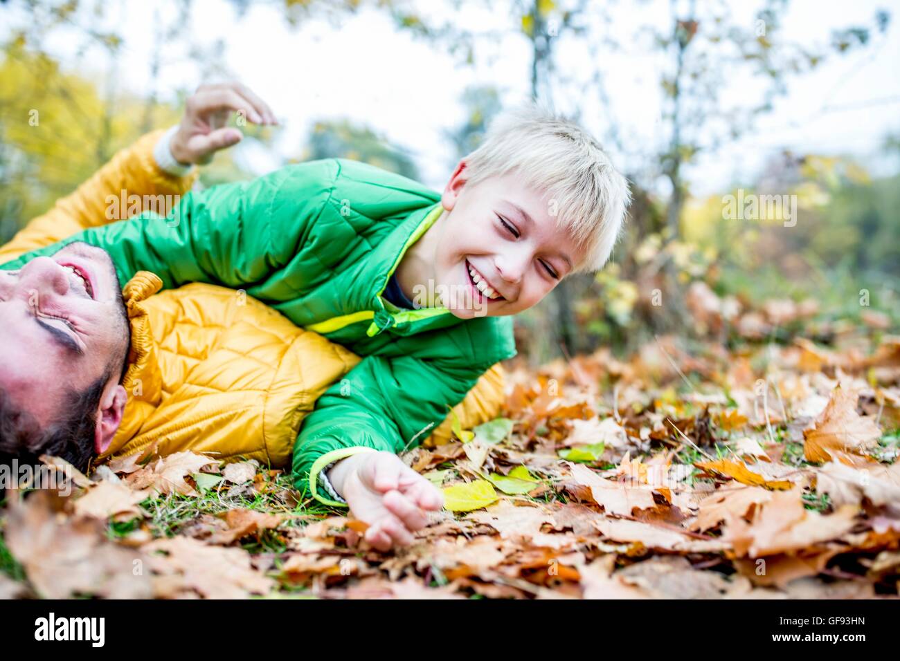 MODEL RELEASED. Father and son lying on dried leaves in autumn and laughing. Stock Photo