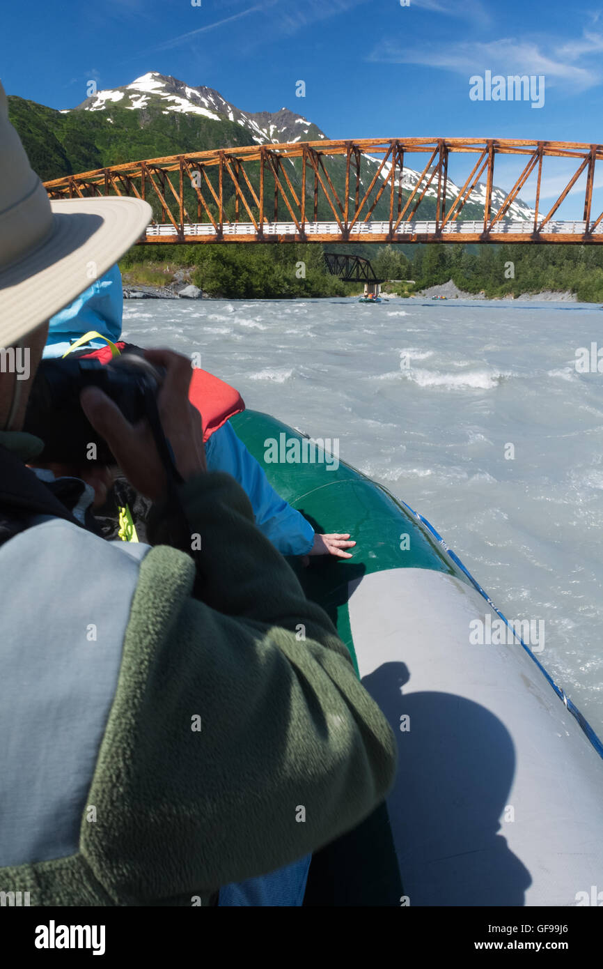 A man tries to take a picture from a raft sweeping down a river towards a bridge. Stock Photo