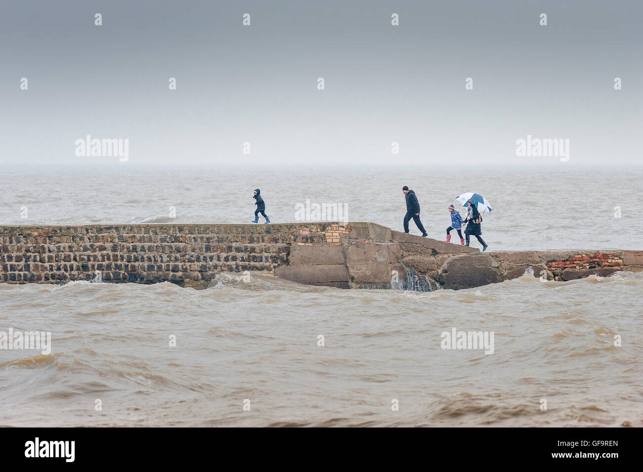Family sea storm stormy danger, a family on a stone jetty hurry back to shore after the weather suddenly deteriorates, Walton,UK Stock Photo