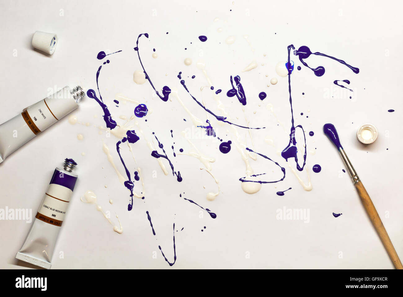 Artistic expression. Blots of purple and white paint on a paper sheet with brush, oil color tubes lying near it. Stock Photo