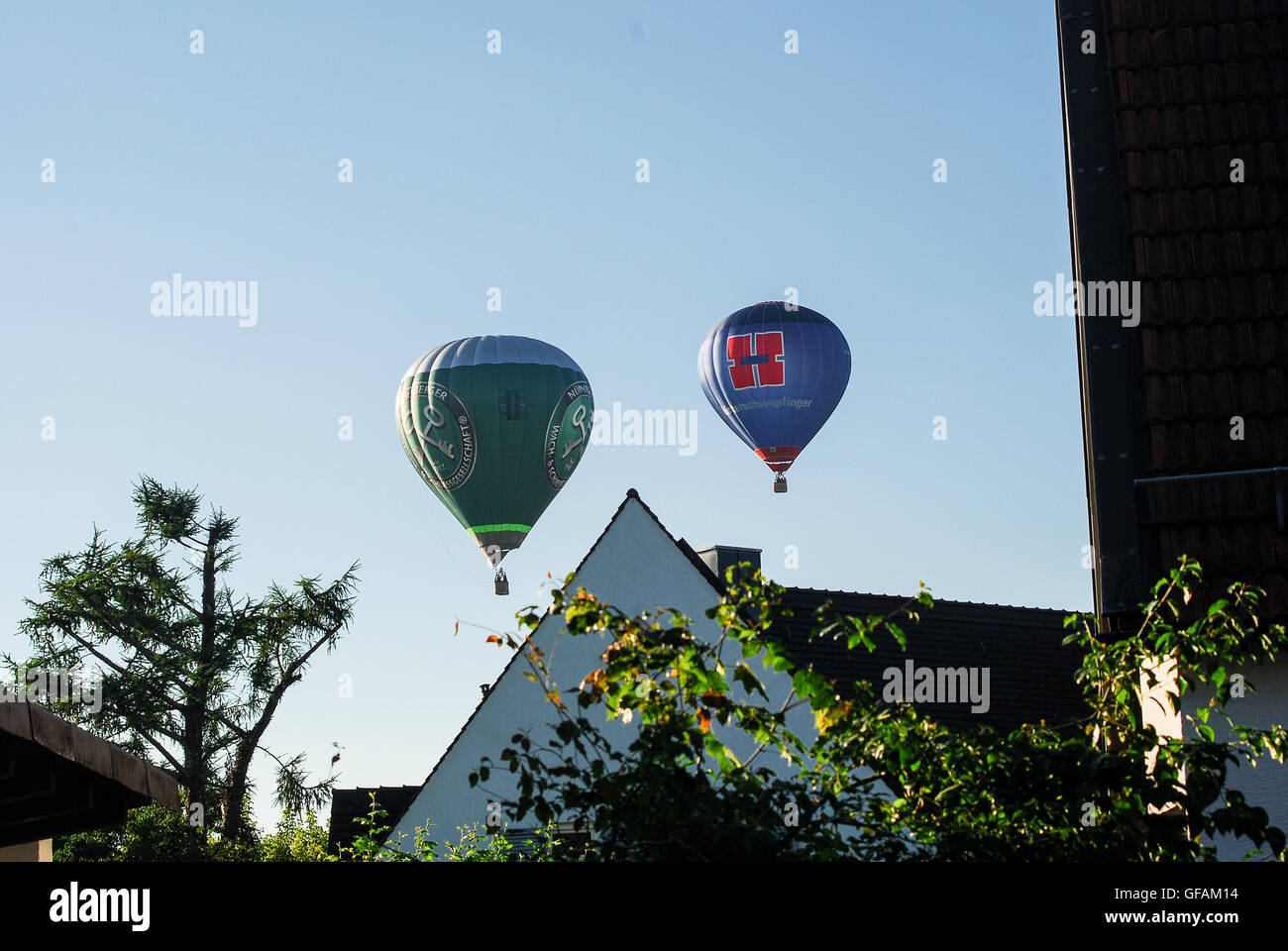 Two hot air balloons fly low over roofs while preparing to land under clear blue sky in Neuötting,Bavaria,Germany Stock Photo